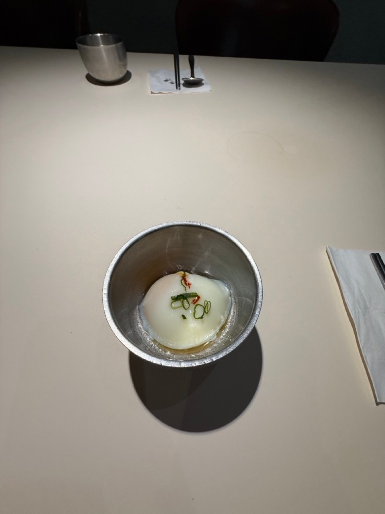 An elegant top-down focus on Wongiok's welcoming appetizer, a traditional soft slow-cooked Korean egg (Suran) served in a neat bowl.
