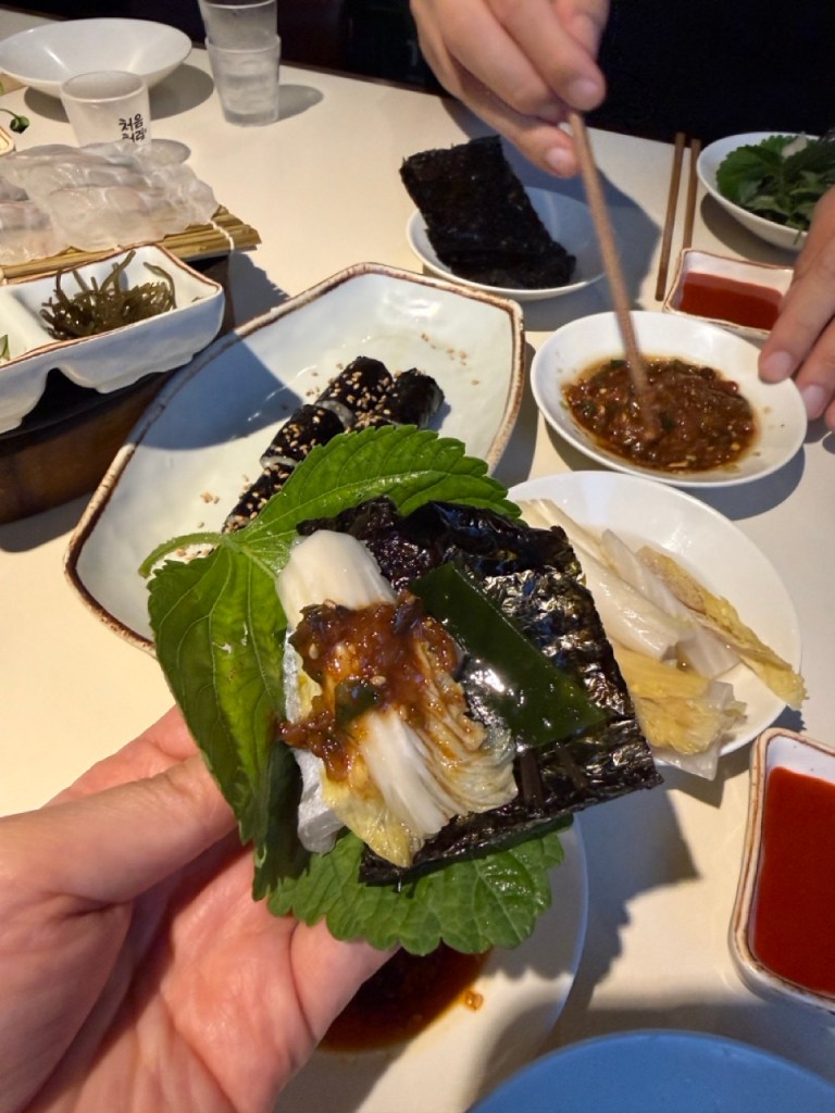 A beautiful close-up of a hand holding a fresh perilla leaf wrap filled with raw fish, garlic, and ssamjang.