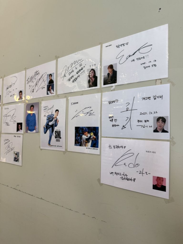 A high-satisfaction macro close-up of handwritten celebrity signatures and warm message ink strokes framed on the wall.
