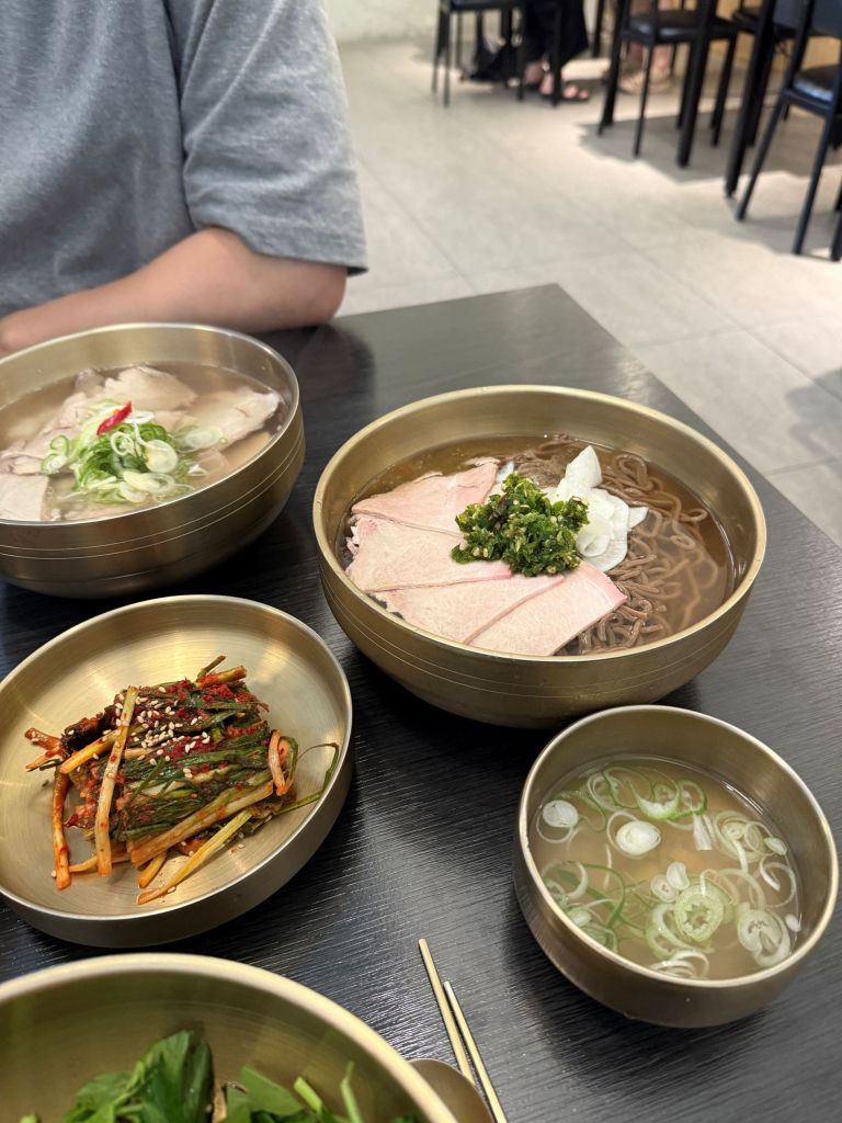 An aesthetic lifestyle snapshot showing fresh cubed radish kimchi and fermented seafood served alongside pork soup.