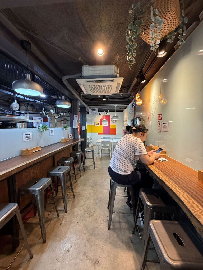 An aesthetic focus on a cozy wooden bar seating corner overlooking a peaceful Seoul Forest alleyway.