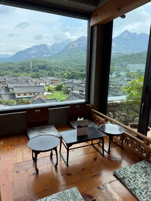 A high-satisfaction top-down view of a modern dining table setup overlooking Eunpyeong Hanok Village and Bukhansan at 1in1sang.