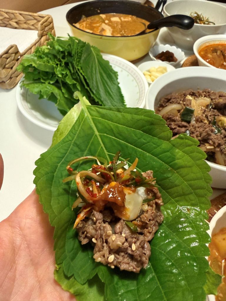 A cinematic focus on a fresh perilla leaf wrap loaded with savory beef bulgogi, sliced raw garlic, and green chili.