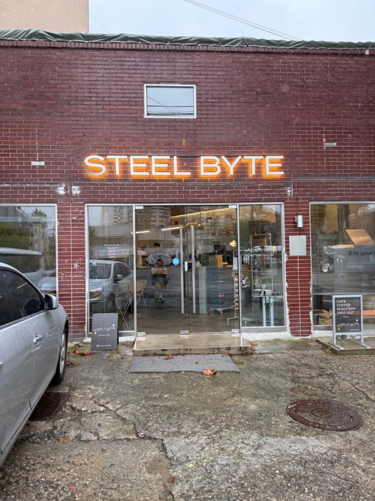A high-satisfaction top-down view of the modern industrial entrance facade and signboard of STEEL BYTE cafe in Mullae.
