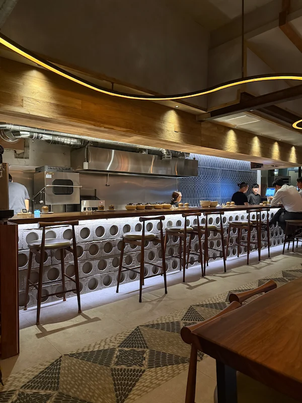 An aesthetic lifestyle snapshot showing a diner enjoying small Korean tapas plates at a cozy dining bar counter.